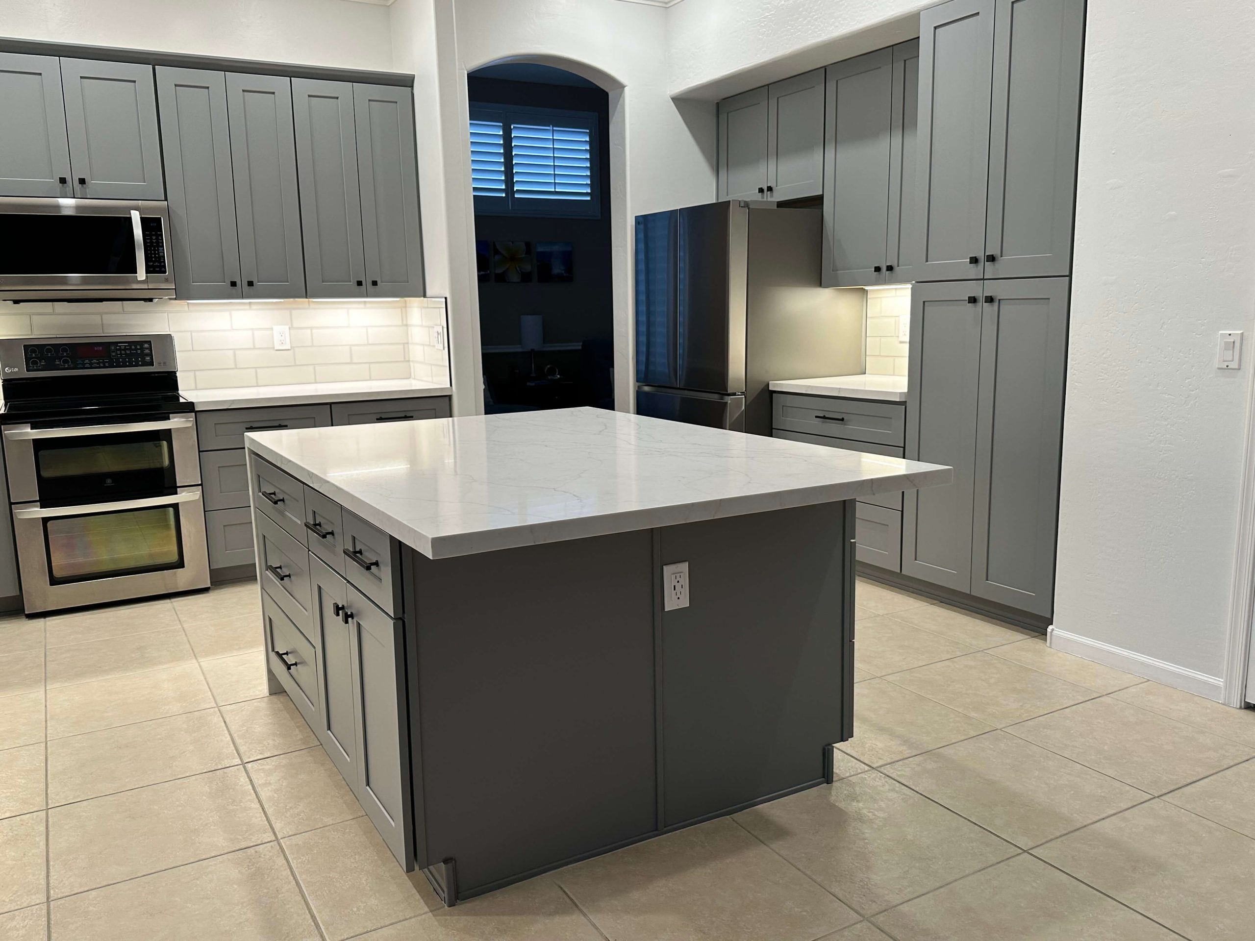 Modern kitchen featuring gray cabinetry, stainless steel appliances, a marble island countertop, and tiled flooring.